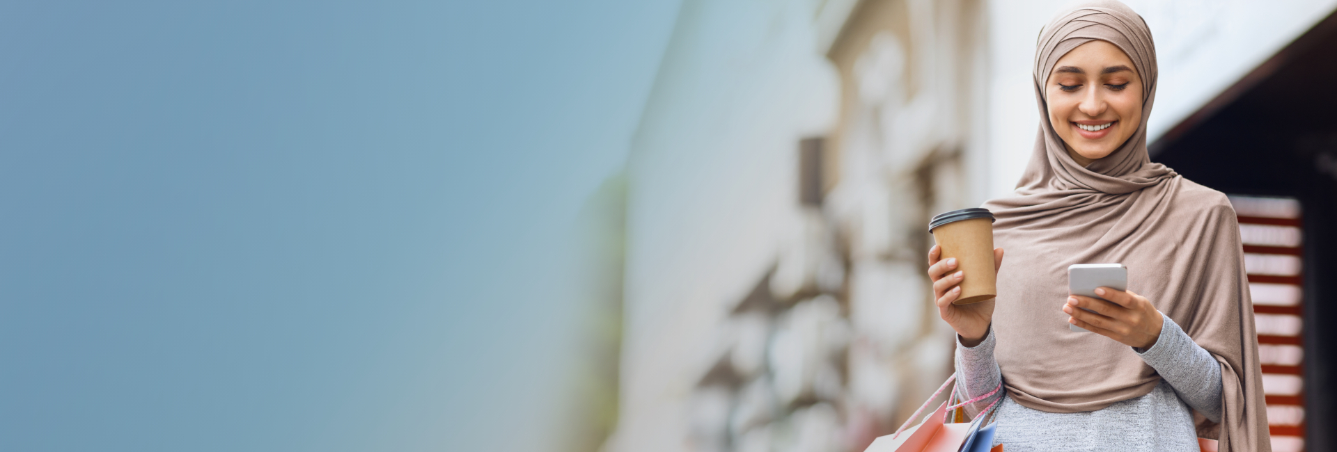 Lady using her phone while holding shopping bags and coffee in her hand  